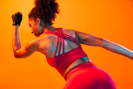 Sportive black hispanic woman wearing sportswear training in fitness studio, colorful dramatic lighting - African-american female athlete doing sport workoutの写真素材