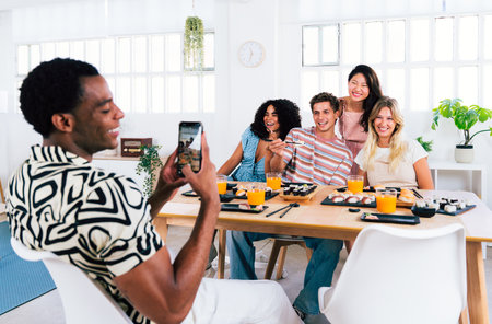 Multiethnic group of young friends meeting at home and eating sushi - Multiracial happy people bonding while having lunchの写真素材