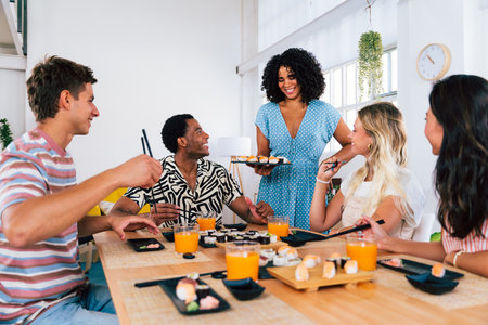 Multiethnic group of young friends meeting at home and eating sushi - Multiracial happy people bonding while having lunchの写真素材