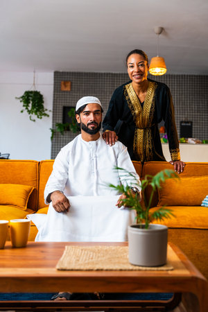 Happy beautiful young arab couple with emirati clothing together at home - Middle-eastern man and woman with traditional arabic attireの写真素材