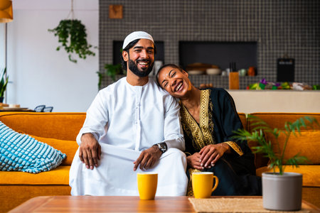 Happy beautiful young arab couple with emirati clothing together at home - Middle-eastern man and woman with traditional arabic attireの写真素材