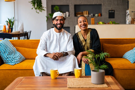 Happy beautiful young arab couple with emirati clothing together at home - Middle-eastern man and woman with traditional arabic attireの写真素材
