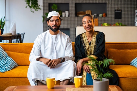 Happy beautiful young arab couple with emirati clothing together at home - Middle-eastern man and woman with traditional arabic attireの写真素材