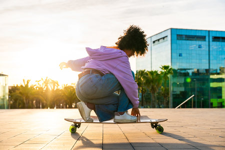 Beautiful young black woman with curly afro hair portrait outdoors - Modern cool female stylish wearing urban clothing strolling in the city dancing on longboardの写真素材