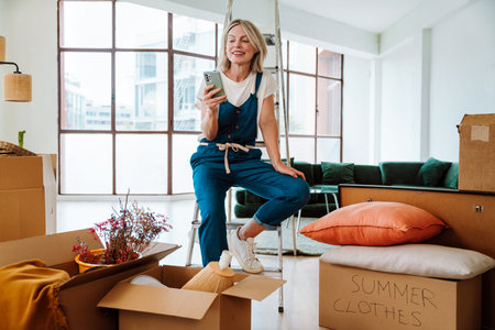 Single woman relocating in a new apartment. Middle aged senior beautiful woman moving boxes and...