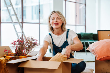 Single woman relocating in a new apartment. Middle aged senior beautiful woman moving boxes and...