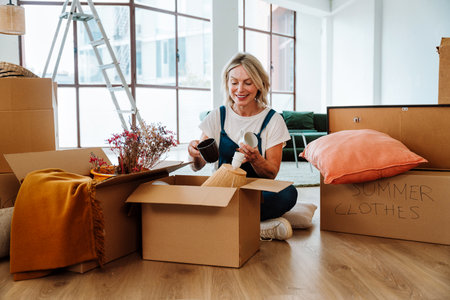 Single woman relocating in a new apartment. Middle aged senior beautiful woman moving boxes and...