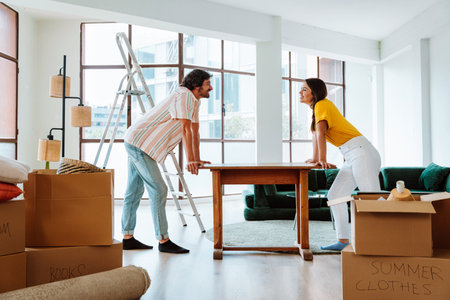 Happy young couple relocating in a new apartment. Young woman and man moving furniture in the new...