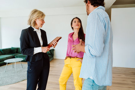 Real estate agent showing a new apartment and features of a good investment to a young couple. Woman and man buying a property in a rich area of the city.の写真素材