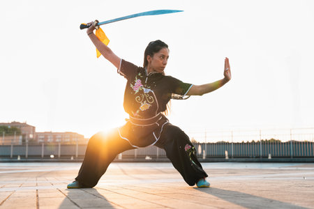Chinese young woman practicing wushu kung fu with weapons outdoor. Young girl training martial arts form for the competition.の写真素材