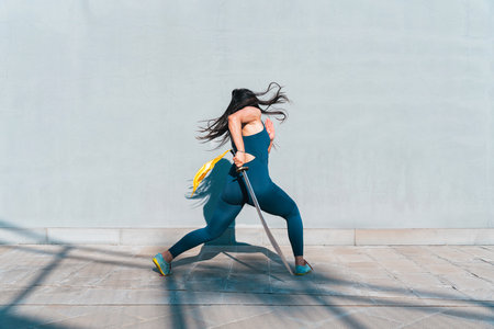 Chinese young woman practicing wushu kung fu with weapons outdoor. Young girl training martial arts form for the competition.の写真素材