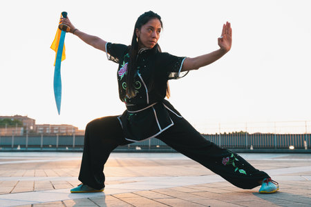 Chinese young woman practicing wushu kung fu with weapons outdoor. Young girl training martial arts form for the competition.の写真素材