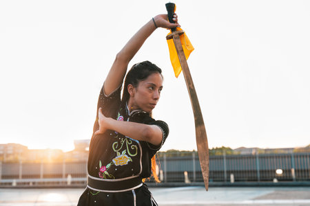 Chinese young woman practicing wushu kung fu with weapons outdoor. Young girl training martial arts...