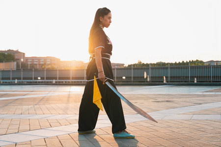 Chinese young woman practicing wushu kung fu with weapons outdoor. Young girl training martial arts...