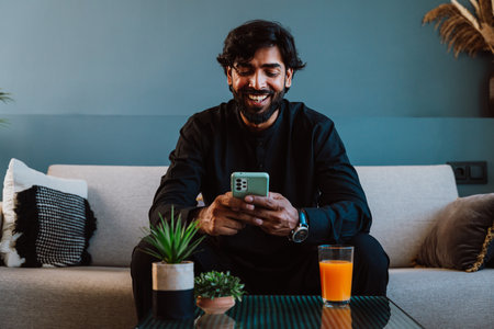 Young man with traditional outfit using smart phone on the couch.