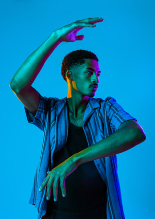 African man young portrait in studio on colorful background - Cool black young male with stylish attire posing, creative colored lightingの写真素材