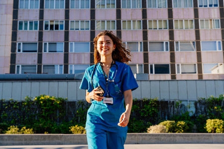 Beautiful young nurse wearing hospital blue uniform strolling in the city - Cheerful caucasian female doctor going to work at the hospitalの写真素材