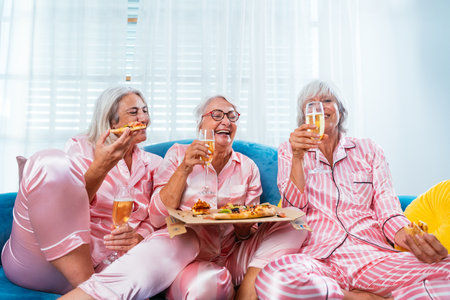 Beautiful senior women having funny pajama party at home - Group of cheerful elderly female friends having fun at home eating pizza, concepts about old people, lifestyle and quality of lifeの写真素材