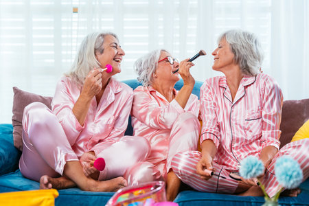 Beautiful senior women having funny pajama party at home - Group of cheerful elderly female friends doing make-up and having fun, concepts about old people, lifestyle and quality of lifeの写真素材