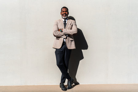 Mature black businessman wearing elegant suit standing against a wall - Corporate african adult senior male with gray beardの写真素材