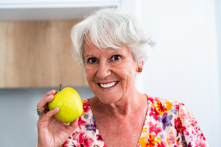 Beautiful senior old woman with gray hair eating fruits at home - Youthful elderly granmother spending quality time at homeの写真素材