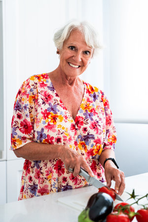 Beautiful senior old woman with gray hair cooking at home - Youthful elderly granmother spending quality time at homeの写真素材