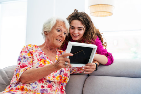 Beautiful grandmother and granddaughter together at home watching family picture - Cheerful...