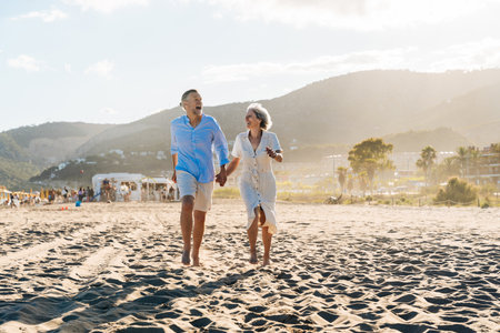 Beautiful happy senior couple dating at the seaside during summertime - Mature married couple in love bonding outdoors at the beach, concepts about elderly lifestyle, relationship and quality of lifeの写真素材