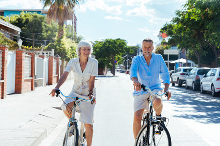 Beautiful happy senior couple dating at the seaside during summertime - Mature married couple in love bonding outdoors and riding bicycle, concepts about elderly lifestyle, transportation and quality of lifeの写真素材