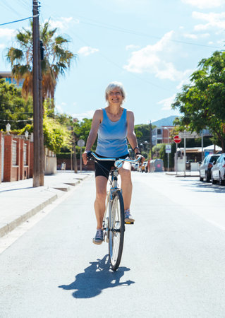 Beautiful happy senior woman cycling during summertime - Mature adult female with gray hair riding bicycle, concepts about elderly lifestyle, transportation and quality of lifeの写真素材