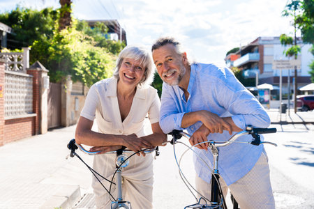 Beautiful happy senior couple at the seaside during summertime - Mature married couple in love bonding outdoors and riding bicycle, concepts about elderly lifestyle, transportation and quality of lifeの写真素材
