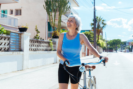 Beautiful happy senior woman cycling during summertime - Mature adult female with gray hair riding bicycle, concepts about elderly lifestyle, transportation and quality of lifeの写真素材