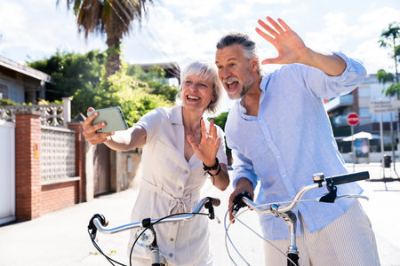 Beautiful happy senior couple dating at the seaside during summertime - Mature married couple in love bonding outdoors and riding bicycle, concepts about elderly lifestyle, transportation and quality of lifeの写真素材