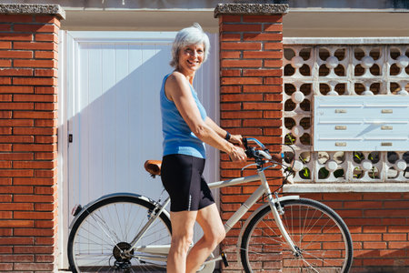 Beautiful happy senior woman cycling during summertime - Mature adult female with gray hair riding bicycle, concepts about elderly lifestyle, transportation and quality of lifeの写真素材