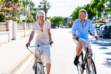 Beautiful happy senior couple at the seaside during summertime - Mature married couple in love bonding outdoors and riding bicycle, concepts about elderly lifestyle, transportation and quality of lifeの写真素材