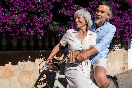 Beautiful happy senior couple dating at the seaside during summertime - Mature married couple in love bonding outdoors and riding bicycle, concepts about elderly lifestyle, transportation and quality of lifeの写真素材
