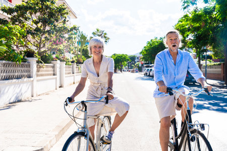 Beautiful happy senior couple dating at the seaside during summertime - Mature married couple in love bonding outdoors and riding bicycle, concepts about elderly lifestyle, transportation and quality of lifeの写真素材