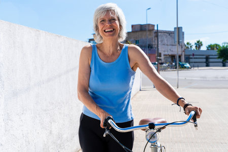Beautiful happy senior woman cycling during summertime - Mature adult female with gray hair riding bicycle, concepts about elderly lifestyle, transportation and quality of lifeの写真素材