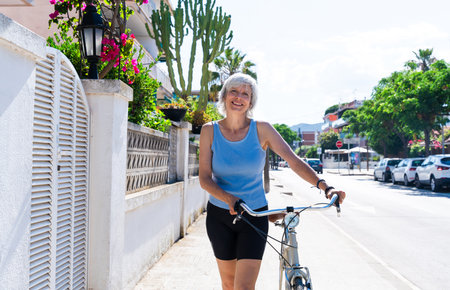 Beautiful happy senior woman cycling during summertime - Mature adult female with gray hair riding bicycle, concepts about elderly lifestyle, transportation and quality of lifeの写真素材