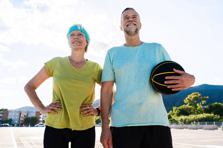 Beautiful happy senior couple playing basketball and having fun - Mature married couple in love bonding outdoors and doing sport together, concepts about elderly lifestyle, relationship and quality of lifeの写真素材