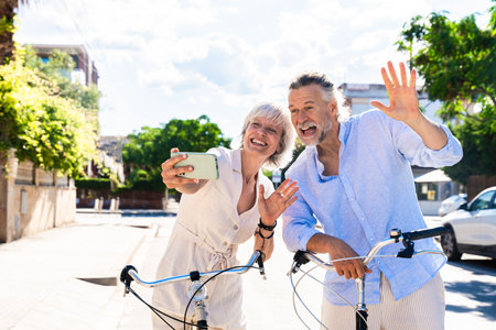Beautiful happy senior couple at the seaside during summertime - Mature married couple in love bonding outdoors and riding bicycle, concepts about elderly lifestyle, transportation and quality of lifeの写真素材