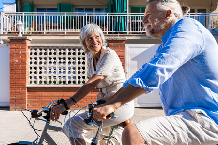 Beautiful happy senior couple at the seaside during summertime - Mature married couple in love bonding outdoors and riding bicycle, concepts about elderly lifestyle, transportation and quality of lifeの写真素材