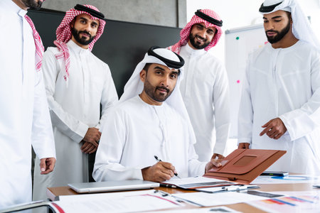Arab businessmen wearing emirati and saudi kandura meeting in office for business deal - Corporate business group of middle-eastern people working in an international company in middle eastの写真素材