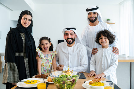 Happy arab family wearing emirati clothing spending time together at home during dinner after...