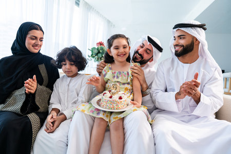 Happy arab family wearing emirati clothing spending time together at home - Middle-eastern parents and children bonding in modern apartment in Dubai celebrating birthdayの写真素材
