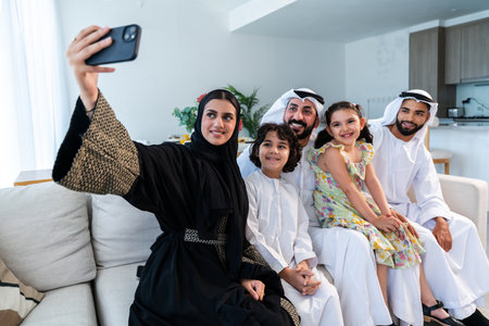 Happy arab family wearing emirati clothing spending time together at home - Middle-eastern parents and children bonding in modern apartment in Dubaiの写真素材