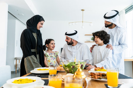 Happy arab family wearing emirati clothing spending time together at home during dinner after...
