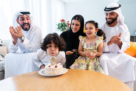 Happy arab family wearing emirati clothing spending time together at home - Middle-eastern parents and children bonding in modern apartment in Dubai celebrating birthdayの写真素材
