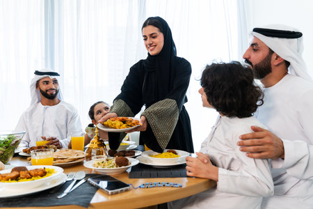 Happy arab family wearing emirati clothing spending time together at home during dinner after ramadan - Middle-eastern parents and children bonding in modern apartment in Dubaiの写真素材