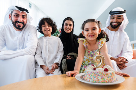 Happy arab family wearing emirati clothing spending time together at home - Middle-eastern parents and children bonding in modern apartment in Dubai celebrating birthdayの写真素材